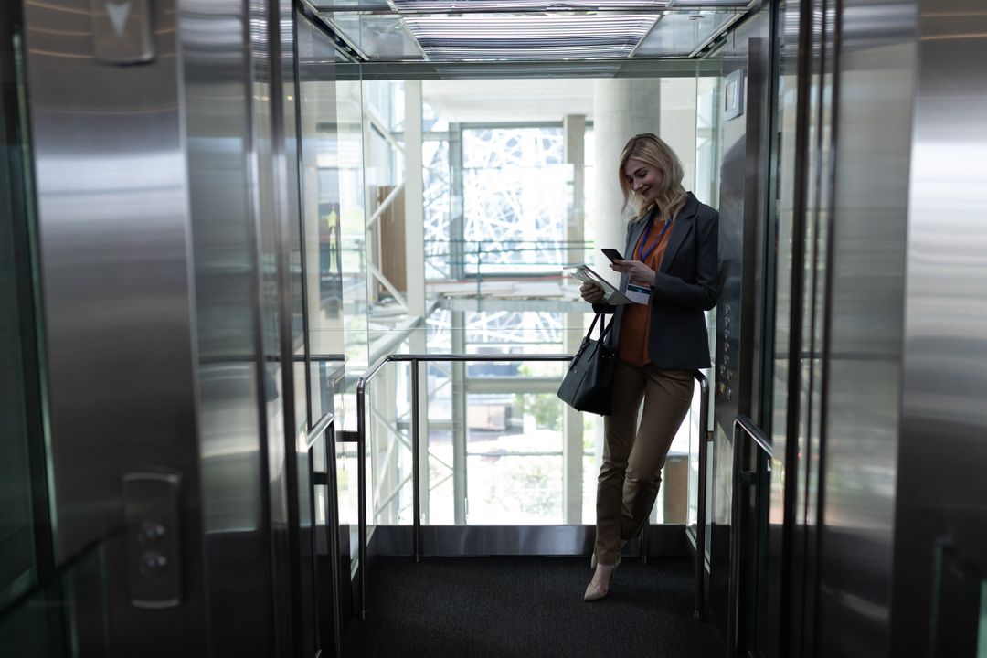 Blonde businesswoman using mobile phone in office elevator - Free Images, Stock Photos and Pictures on Pikwizard.com
