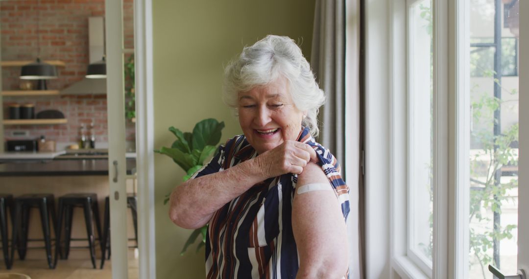 Happy Elderly Woman Showing Vaccination Bandage at Home - Free Images, Stock Photos and Pictures on Pikwizard.com