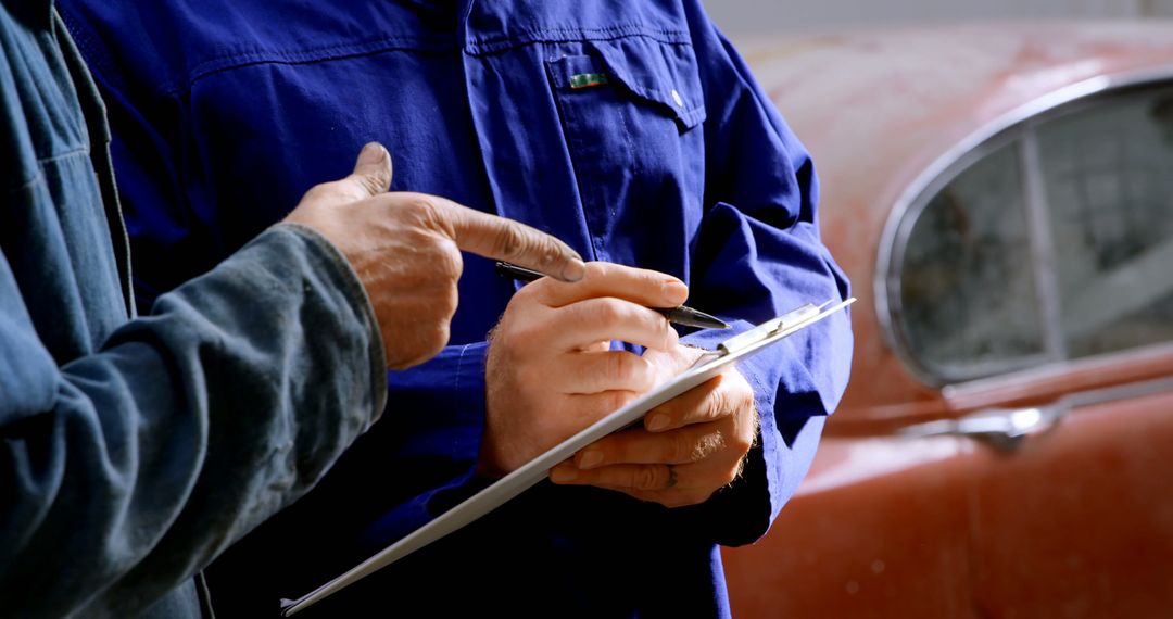 Mechanics Discussing Car Repair Task with Clipboard in Garage - Free Images, Stock Photos and Pictures on Pikwizard.com