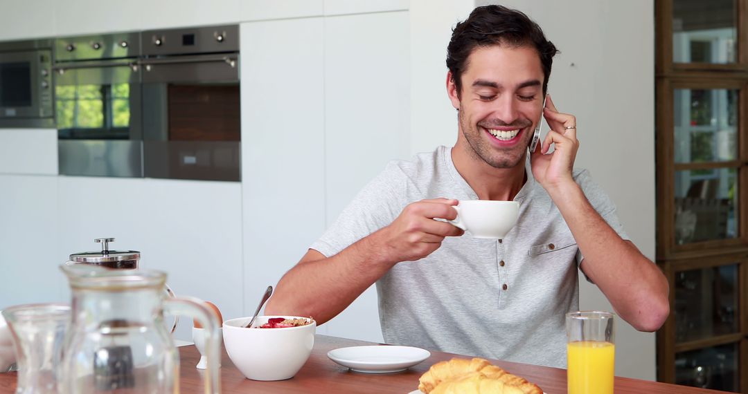 Smiling Man Enjoying Breakfast While Taking Phone Call in Modern Kitchen - Free Images, Stock Photos and Pictures on Pikwizard.com