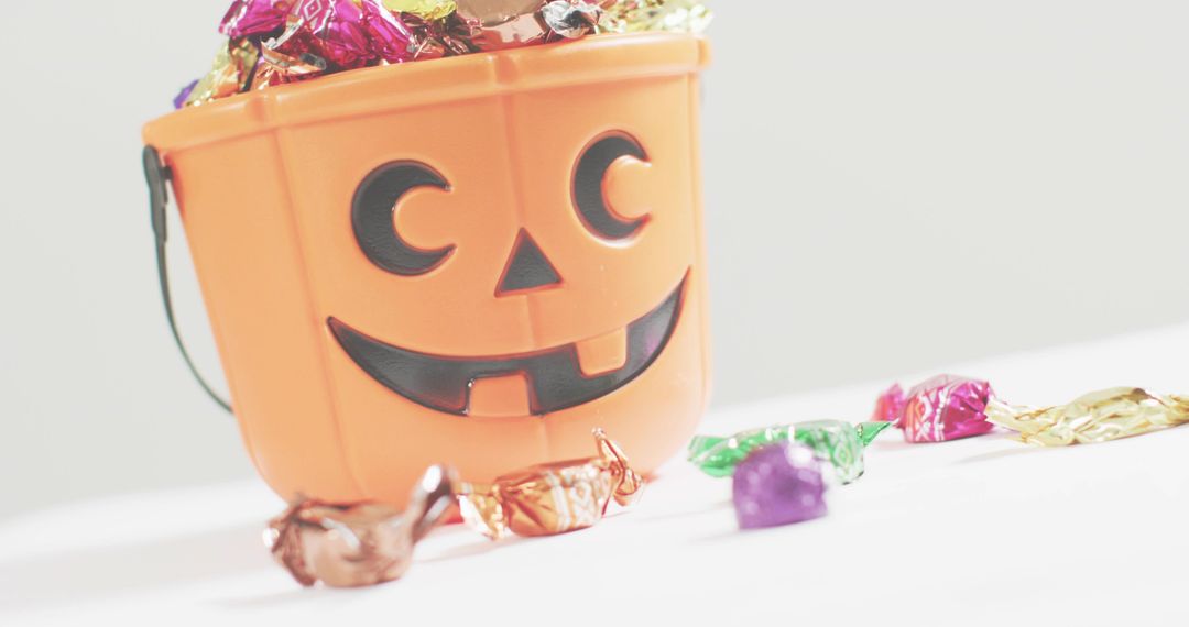 Spilling Halloween candy from jack-o-lantern bucket on white background, copy space