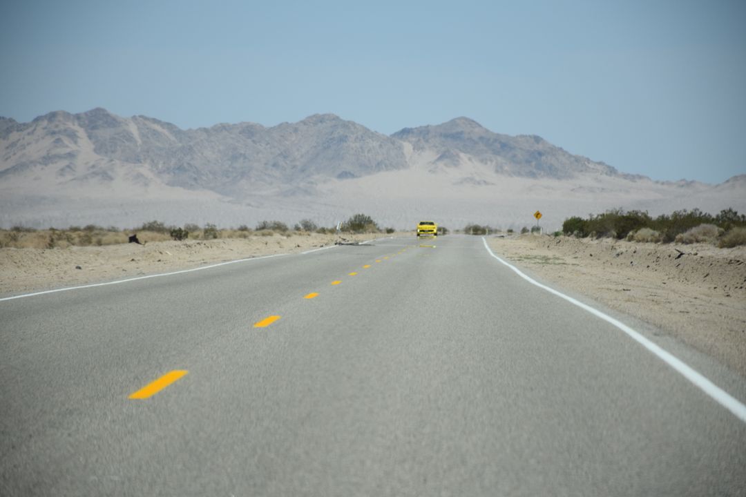 Lone Yellow Car Traveling Desert Highway Towards Mountains - Free Images, Stock Photos and Pictures on Pikwizard.com