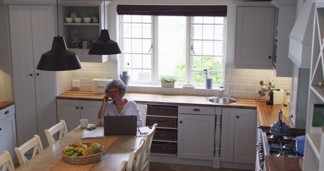 Senior Woman with Laptop Using Phone in Cozy Kitchen - Free Images, Stock Photos and Pictures on Pikwizard.com