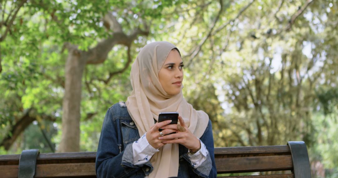 Serene Muslim Woman Enjoying Smartphone in Park - Free Images, Stock Photos and Pictures on Pikwizard.com