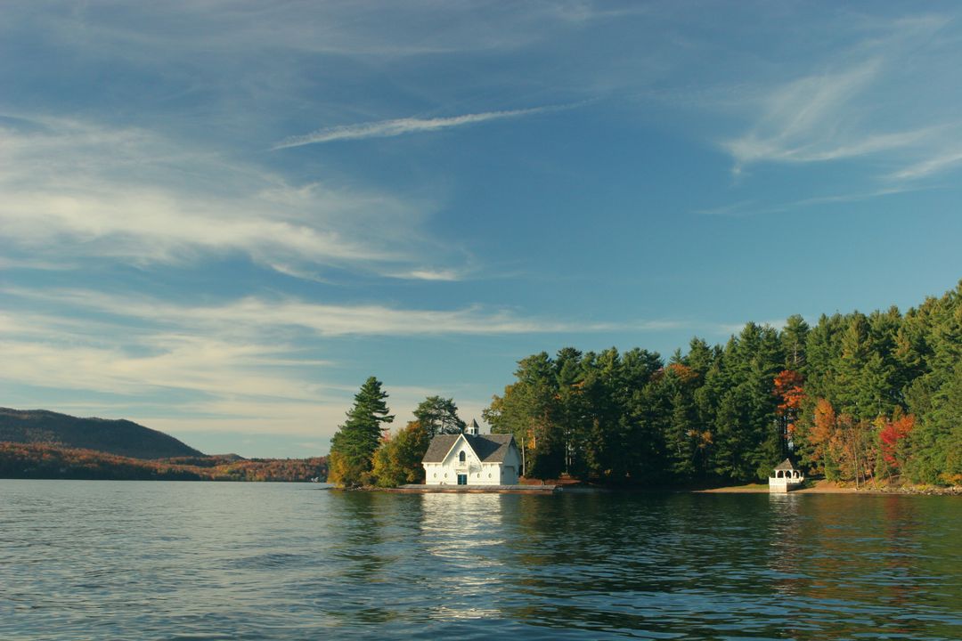 White boathouse sitting on tranquil forest lake with autumn foliage and waterfront gazebo