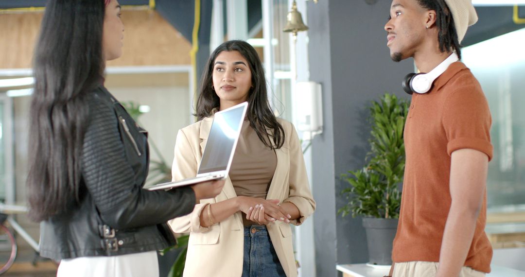 Diverse coworkers discussing project in modern coworking office with laptop and headphones