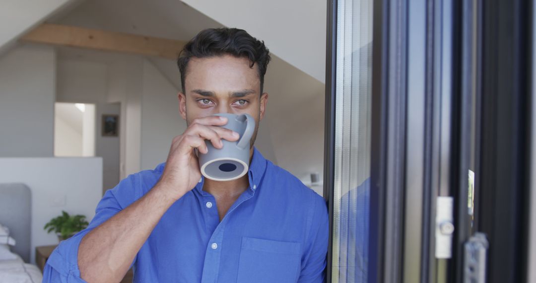 Relaxed Man Wearing Blue Shirt Drinking Coffee by Window - Free Images, Stock Photos and Pictures on Pikwizard.com