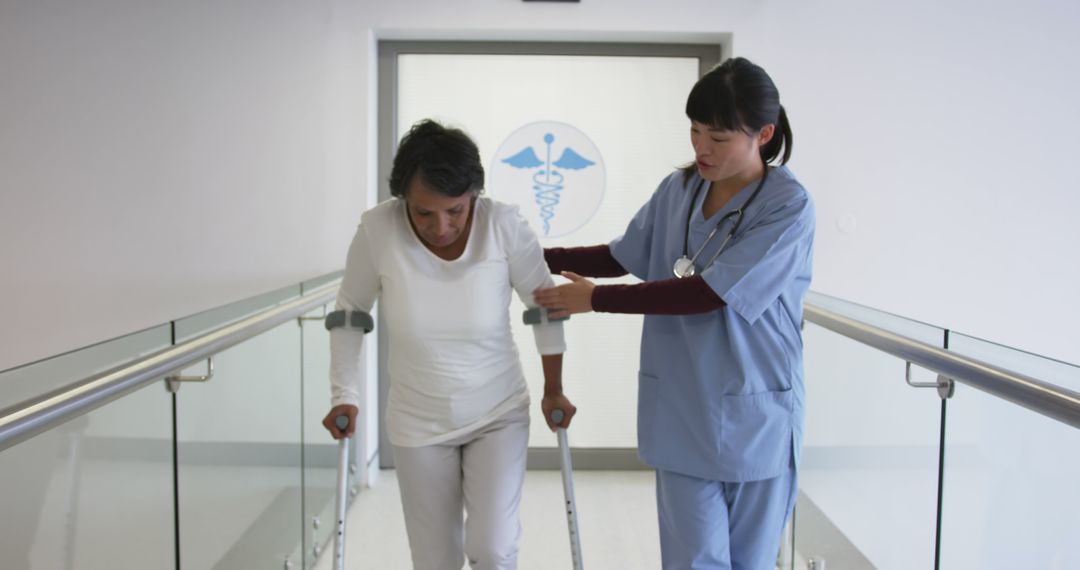 Nurse Assisting Elderly Woman Walking with Crutches in Hospital Corridor - Free Images, Stock Photos and Pictures on Pikwizard.com