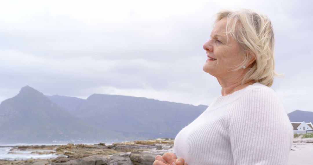 Elderly Woman Enjoying Peaceful Beach View and Mountains - Free Images, Stock Photos and Pictures on Pikwizard.com