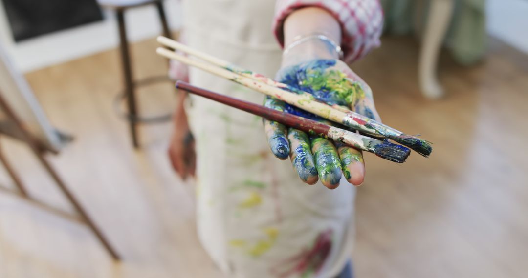 Artist Holding Paintbrushes with Paint-Splattered Hand in Studio - Free Images, Stock Photos and Pictures on Pikwizard.com