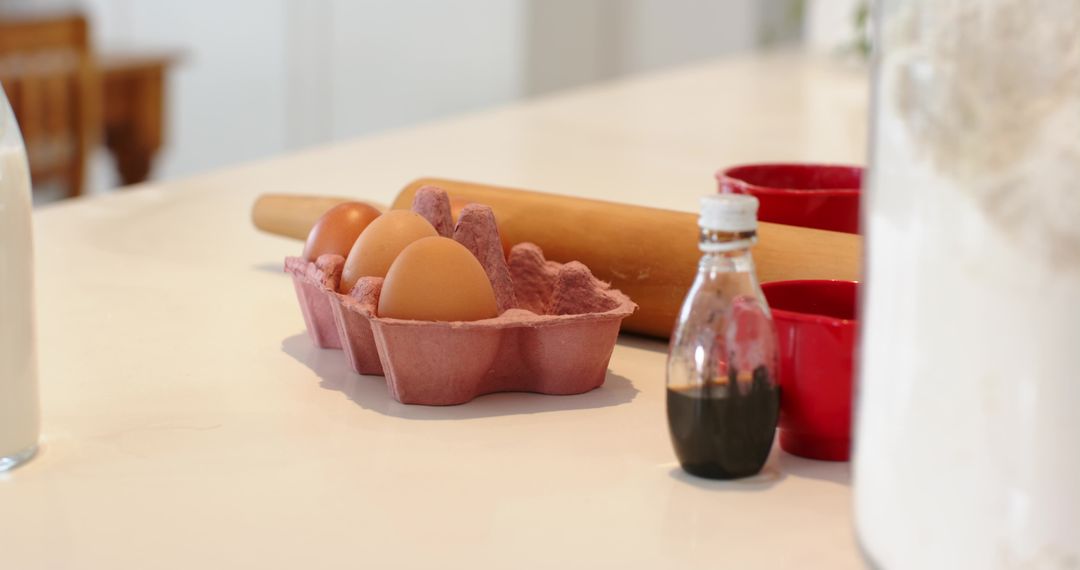 Brown Eggs Resting Beside Pink Carton, Rolling Pin, Vanilla Bottle, Flour on White Countertop