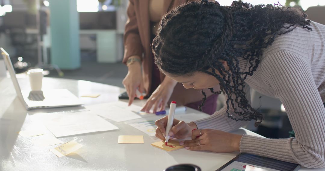 Diverse female coworkers collaborating with sticky notes during office brainstorming