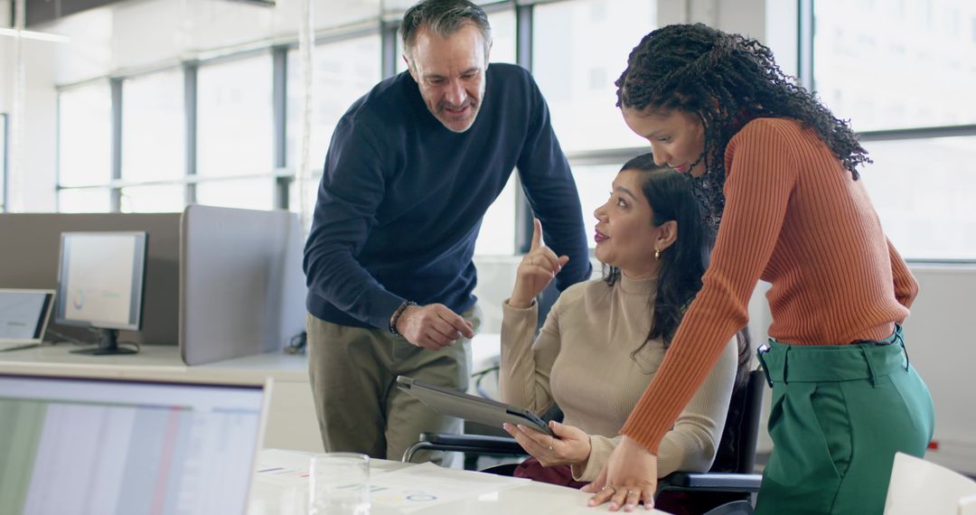 Multicultural team collaborating around tablet and charts in modern open-plan office