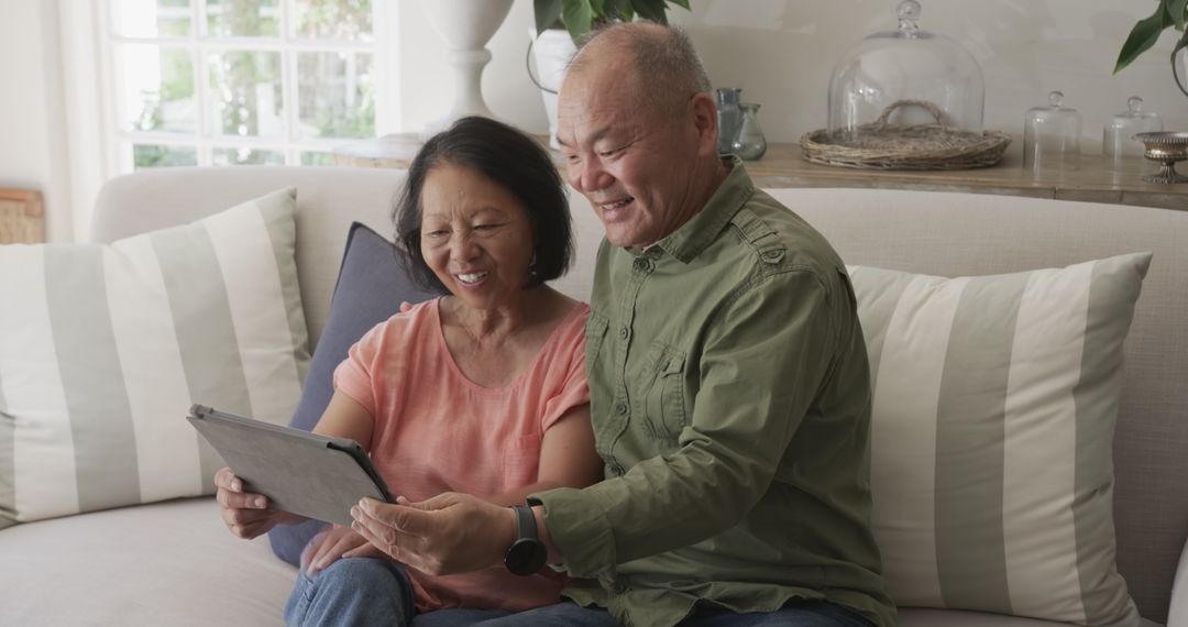 Asian Senior Couple Using Tablet Joyfully at Home