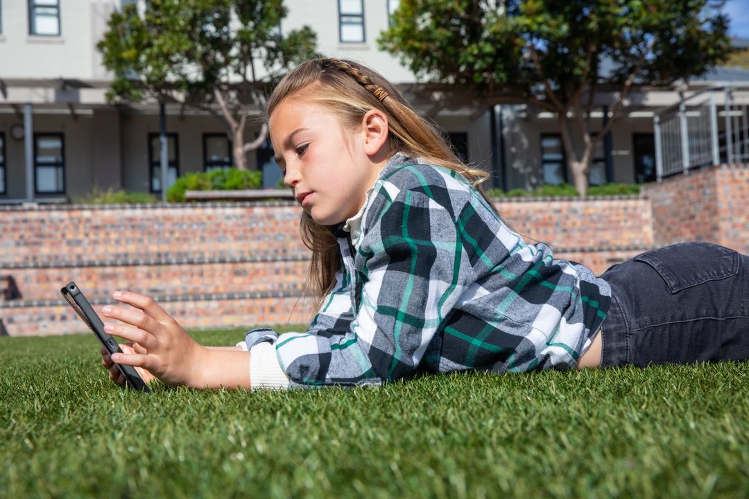 School-age Girl Using Touchscreen Device on Campus Lawn