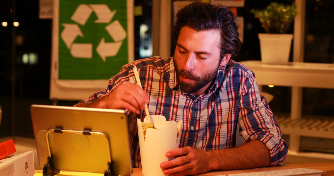 Man Enjoying Takeout Noodles While Working at Night in Eco-Friendly Office - Free Images, Stock Photos and Pictures on Pikwizard.com