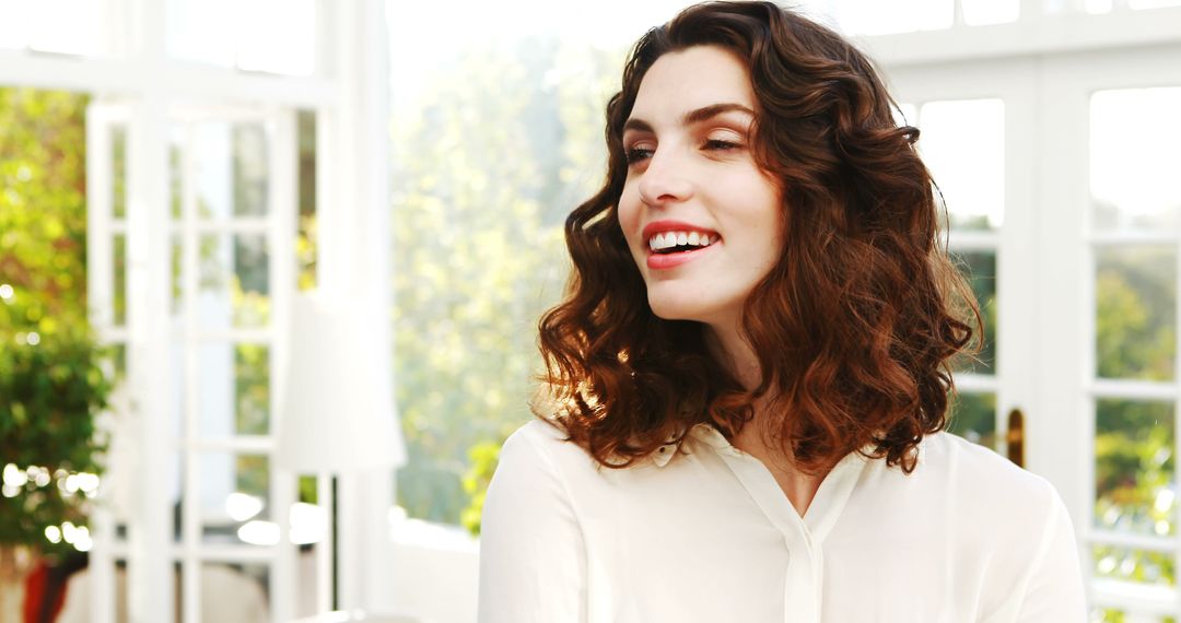 Smiling Woman with Curly Hair in Bright Room with Large Windows - Free Images, Stock Photos and Pictures on Pikwizard.com