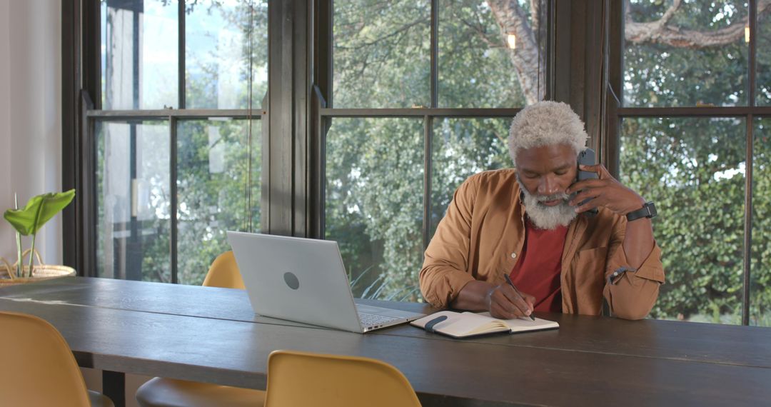 Senior Man Multitasking with Phone and Notebook in Home Office