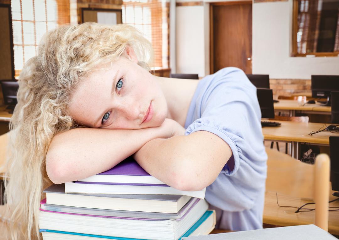 Portrait of a girl resting her head on stack of books in classroom - Free Images, Stock Photos and Pictures on Pikwizard.com
