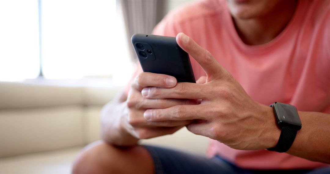 Young Man Engaged with Smartphone Wearing Smartwatch Indoors