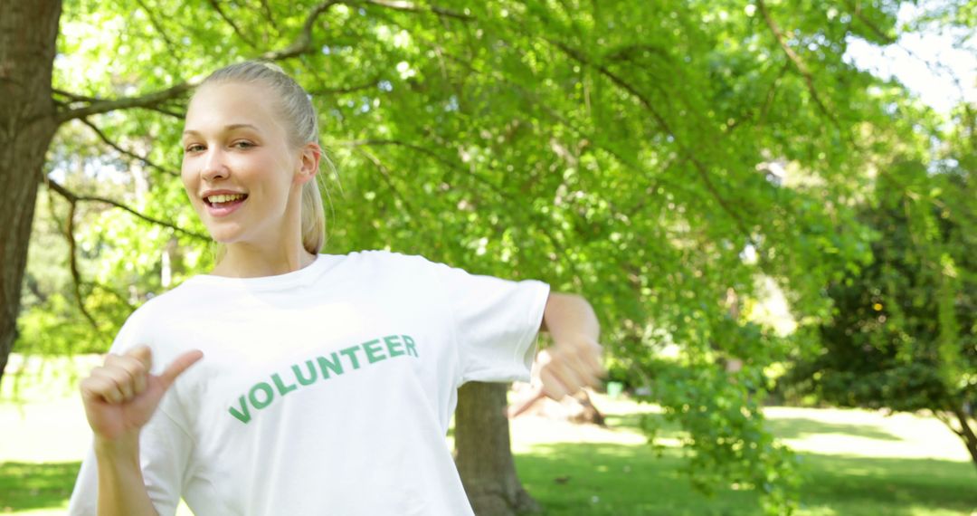 Cheerful Volunteer Smiling and Pointing at Printed Shirt in Park - Free Images, Stock Photos and Pictures on Pikwizard.com