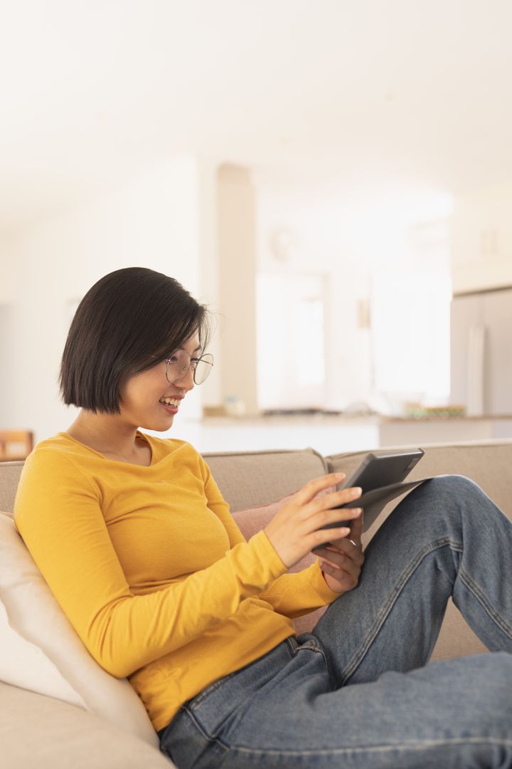 Happy Asian Woman Using Tablet in Living Room - Free Images, Stock Photos and Pictures on Pikwizard.com