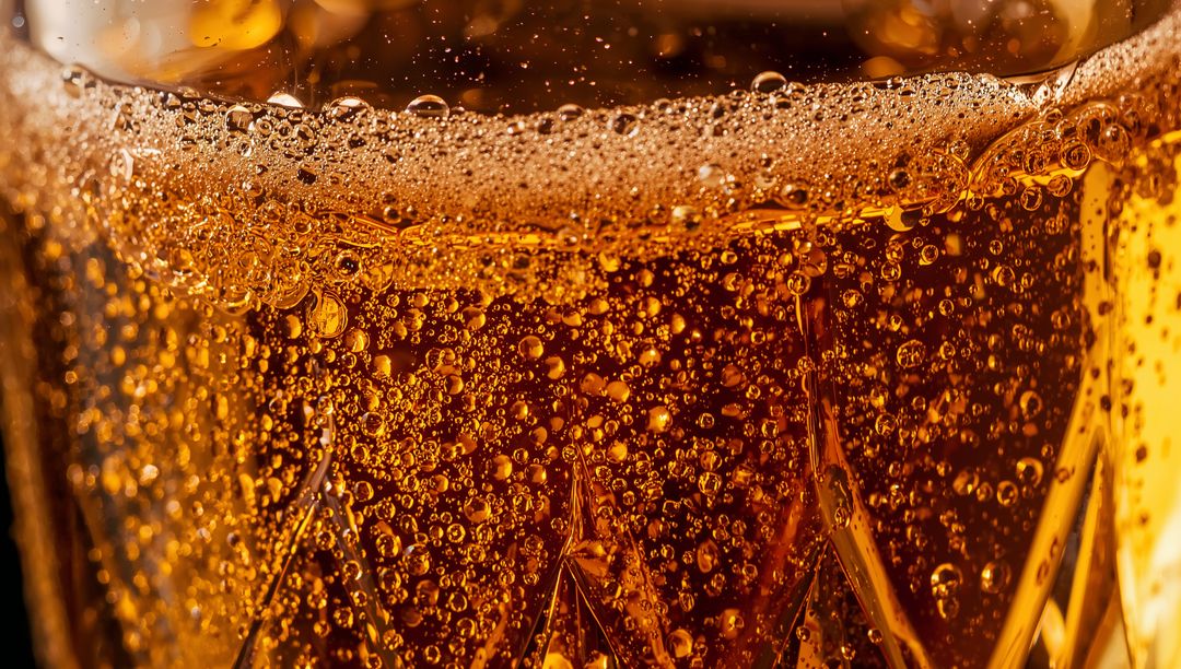 Macro showcasing effervescent amber drink in faceted tumbler with rising bubbles