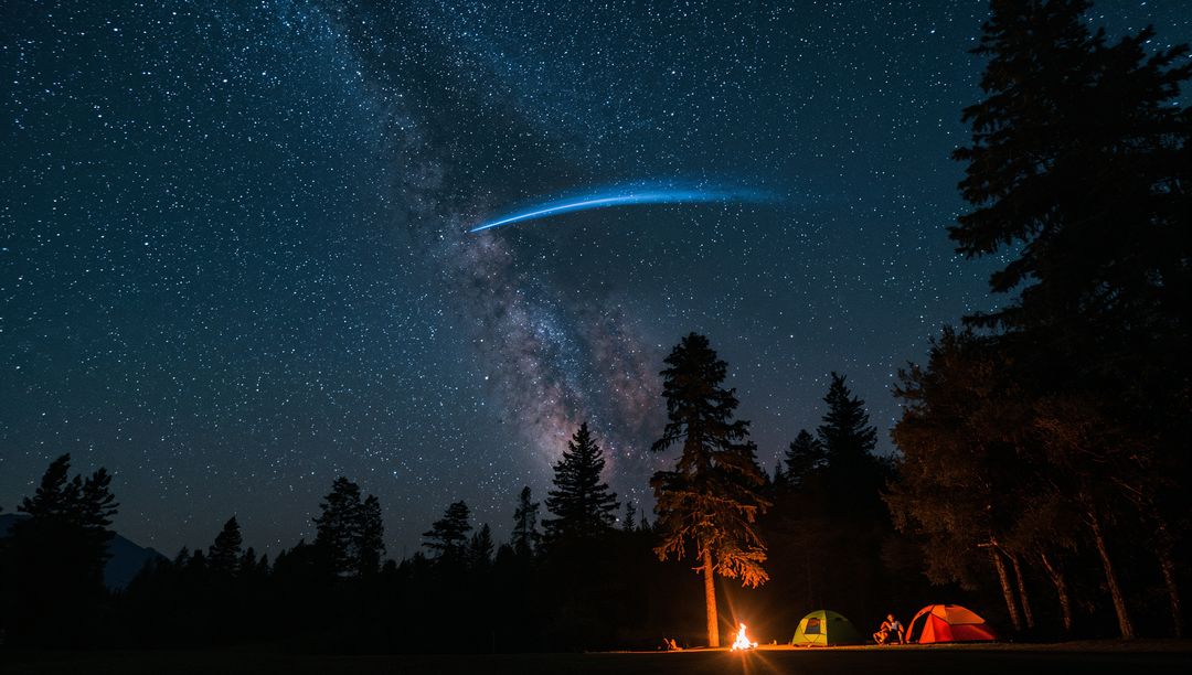 Campers Warming by Campfire Under Milky Way with Meteor Streak and Tents