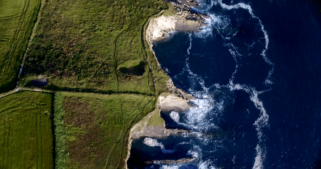 Transparent Waves Crashing against Rocky Coastal Cliffs on Sunny Day