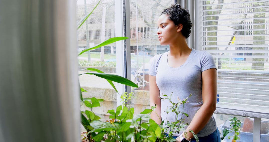 Thoughtful Woman Standing Near Bright Window with Houseplants - Free Images, Stock Photos and Pictures on Pikwizard.com