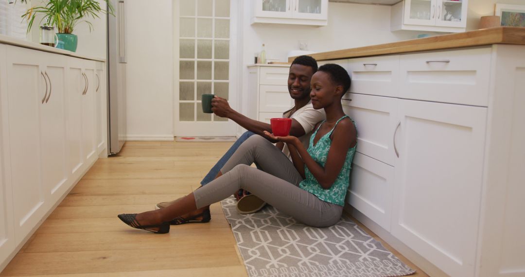 African american couple sitting on kitchen floor drinking coffee and talking - Free Images, Stock Photos and Pictures on Pikwizard.com