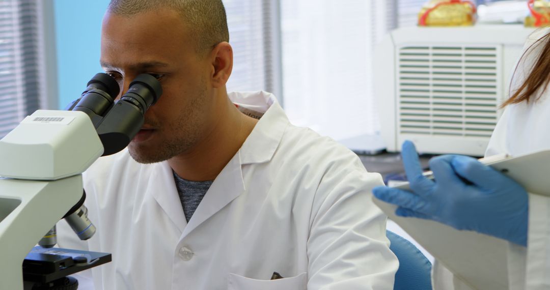 Scientist Analyzing Samples Under Microscope in Collaborative Lab Environment - Free Images, Stock Photos and Pictures on Pikwizard.com