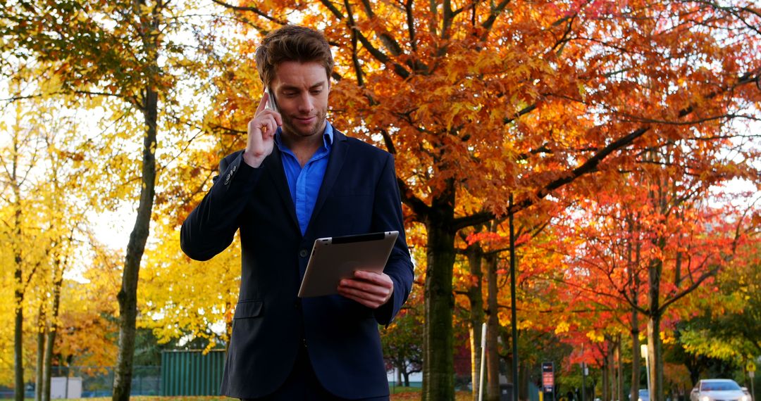 Businessman multitasking with tablet and phone in autumn park - Free Images, Stock Photos and Pictures on Pikwizard.com