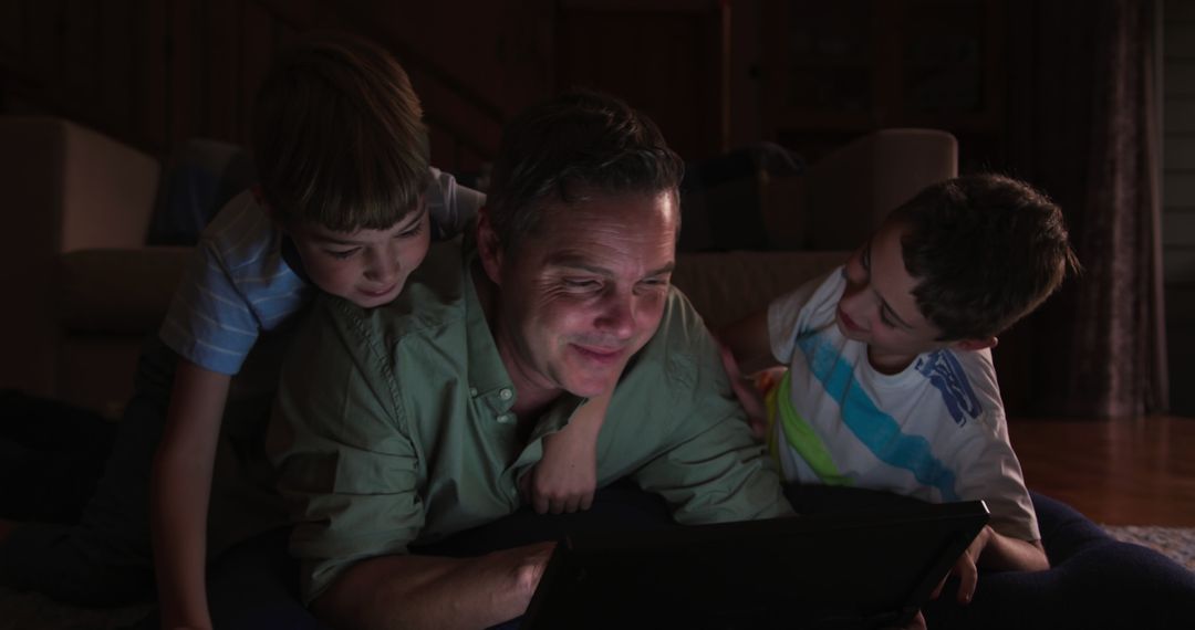 Father and Sons Watching Tablet Screen in Dark Living Room - Free Images, Stock Photos and Pictures on Pikwizard.com