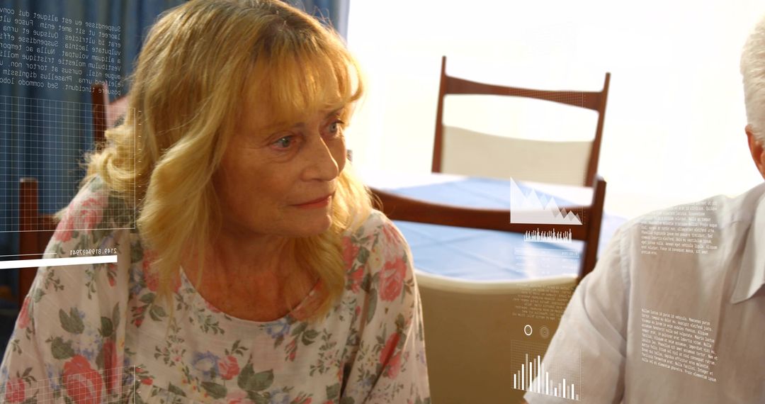 Senior woman sitting at dining table turning toward companion with data and chart overlays