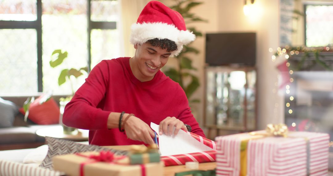 Smiling Young Man Wrapping Christmas Gifts at Home Festive Holiday Season - Free Images, Stock Photos and Pictures on Pikwizard.com