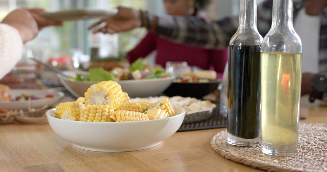 Diverse friends passing bowl of corn and salad at casual family-style dining table