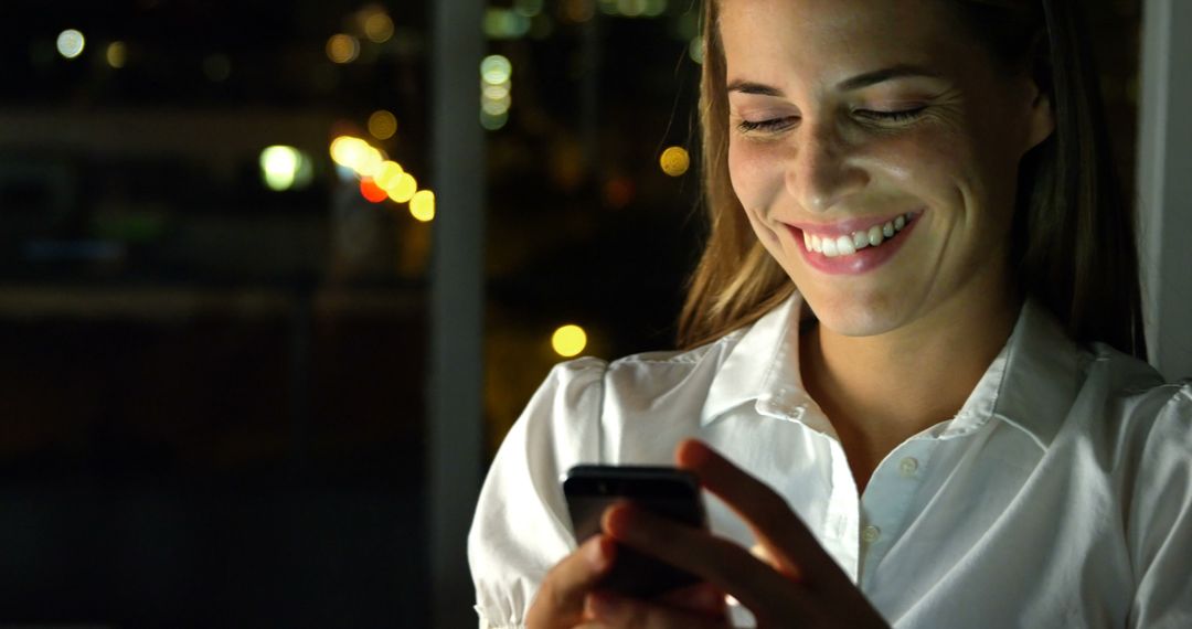 Woman Smiling While Using Smartphone at Night Near Window - Free Images, Stock Photos and Pictures on Pikwizard.com