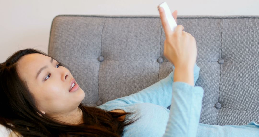 Young Woman Relaxing on Sofa Using Smartphone in Casual Wear - Free Images, Stock Photos and Pictures on Pikwizard.com