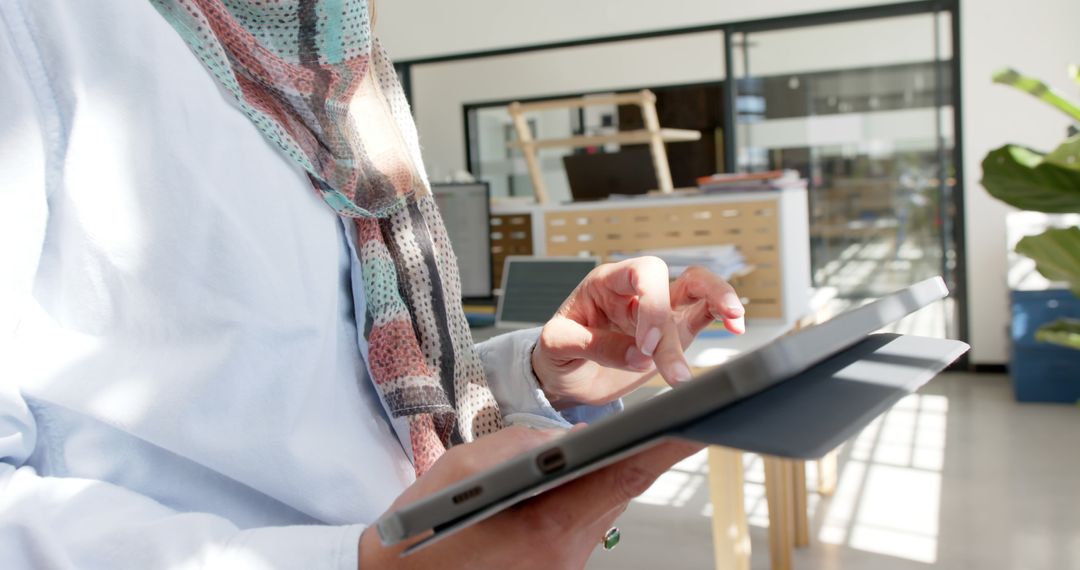 Woman in headscarf using digital tablet in modern office setting