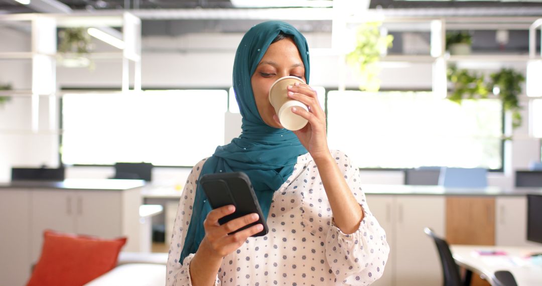 Muslim Woman Drinking Coffee in Modern Office While Using Smartphone - Free Images, Stock Photos and Pictures on Pikwizard.com