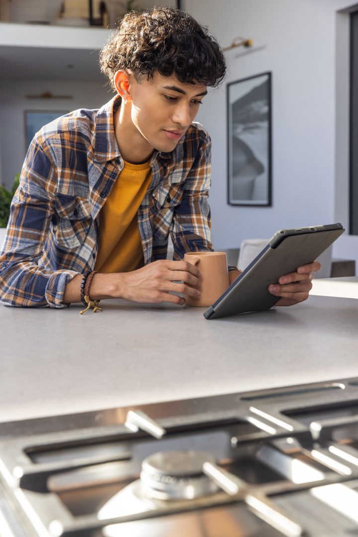 Young Asian Man Relaxing with Coffee and Tablet in Modern Kitchen