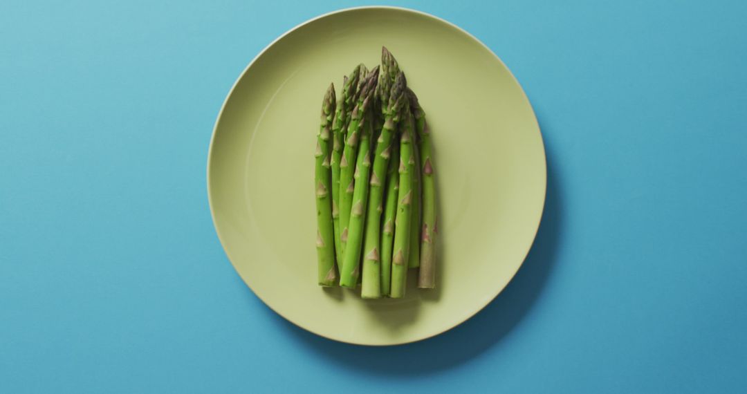 Image of fresh asparagus on green plate over blue background - Free Images, Stock Photos and Pictures on Pikwizard.com