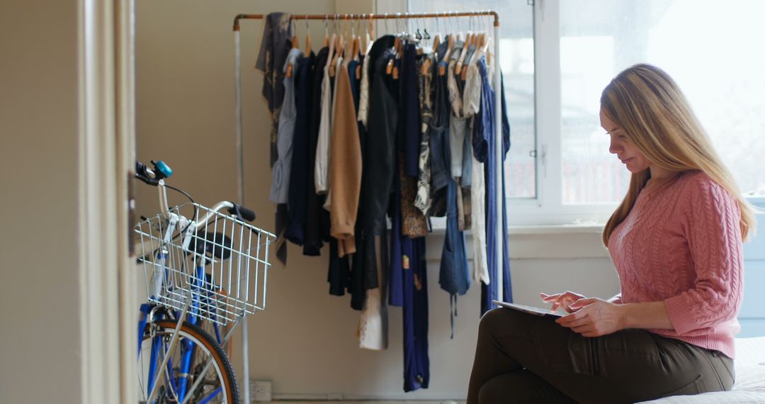 Woman Working on Tablet in Home Office with Clothing Rack and Bicycle - Free Images, Stock Photos and Pictures on Pikwizard.com