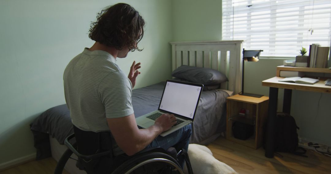 Man in wheelchair working on laptop in minimalist bedroom - Free Images, Stock Photos and Pictures on Pikwizard.com