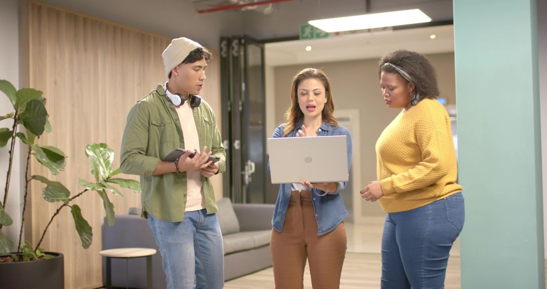 Diverse coworkers discussing project around open laptop in modern office lounge
