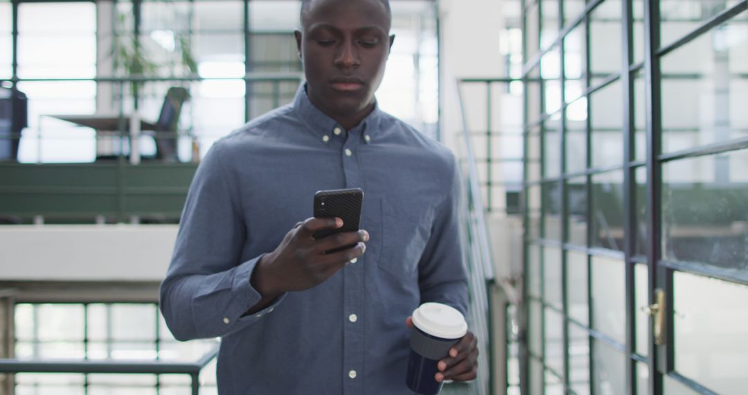 Young Professional Checking Smartphone While Holding Coffee in Modern Office - Free Images, Stock Photos and Pictures on Pikwizard.com