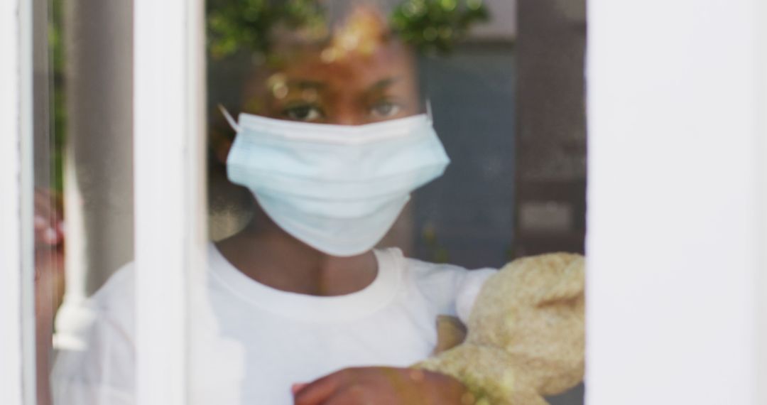 Child in Protective Mask Holding Teddy Bear Looking Through Window - Free Images, Stock Photos and Pictures on Pikwizard.com