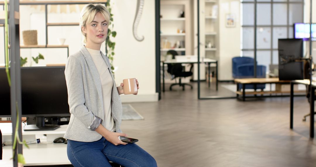 Casually Dressed Businesswoman in Modern Open Office with Coffee and Smartphone