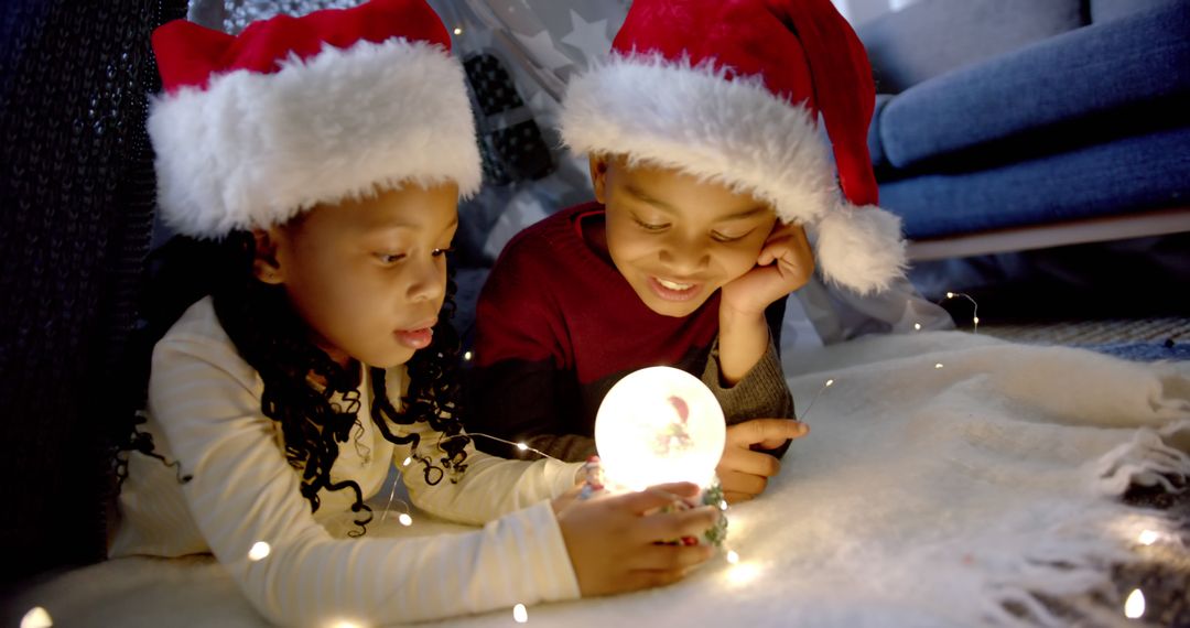 Children with Santa Hats Admiring Illuminated Snow Globe - Free Images, Stock Photos and Pictures on Pikwizard.com